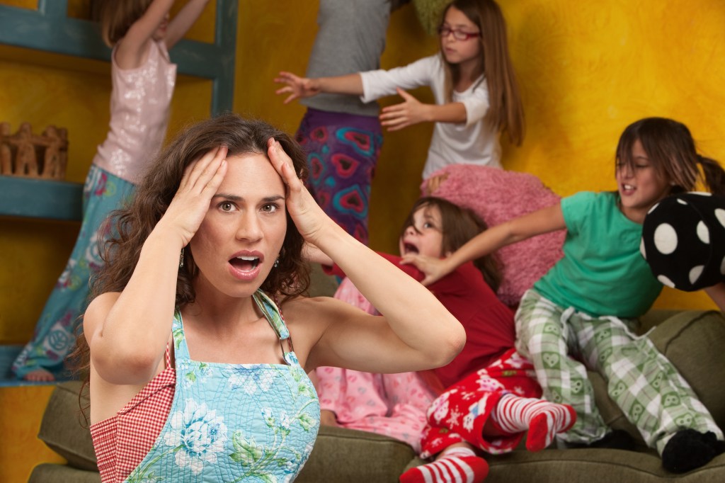 Annoyed mother with hands on head among mischievous little girls